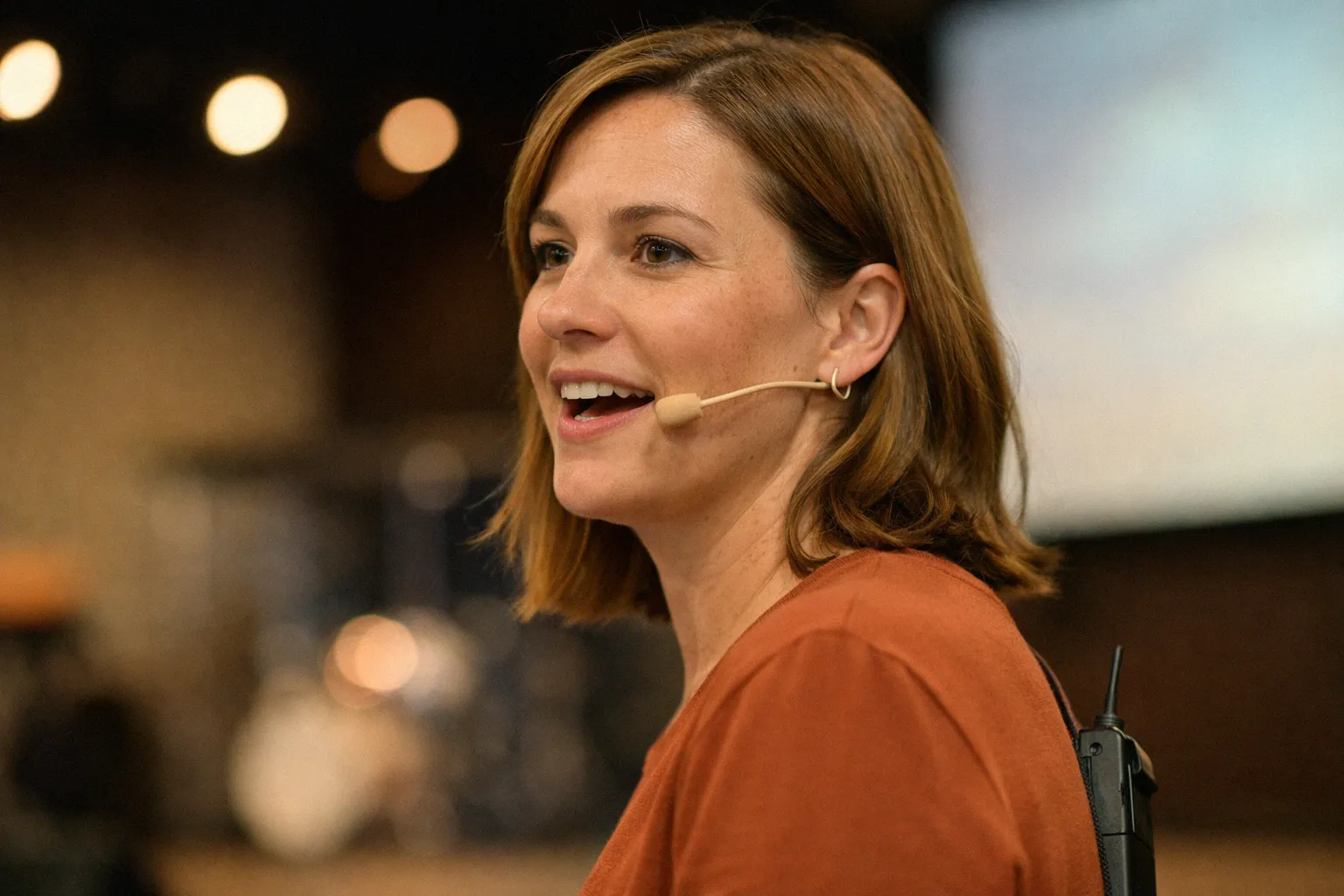 Woman wearing a skin-tone headset microphone with thin boom arm while speaking on a conference stage